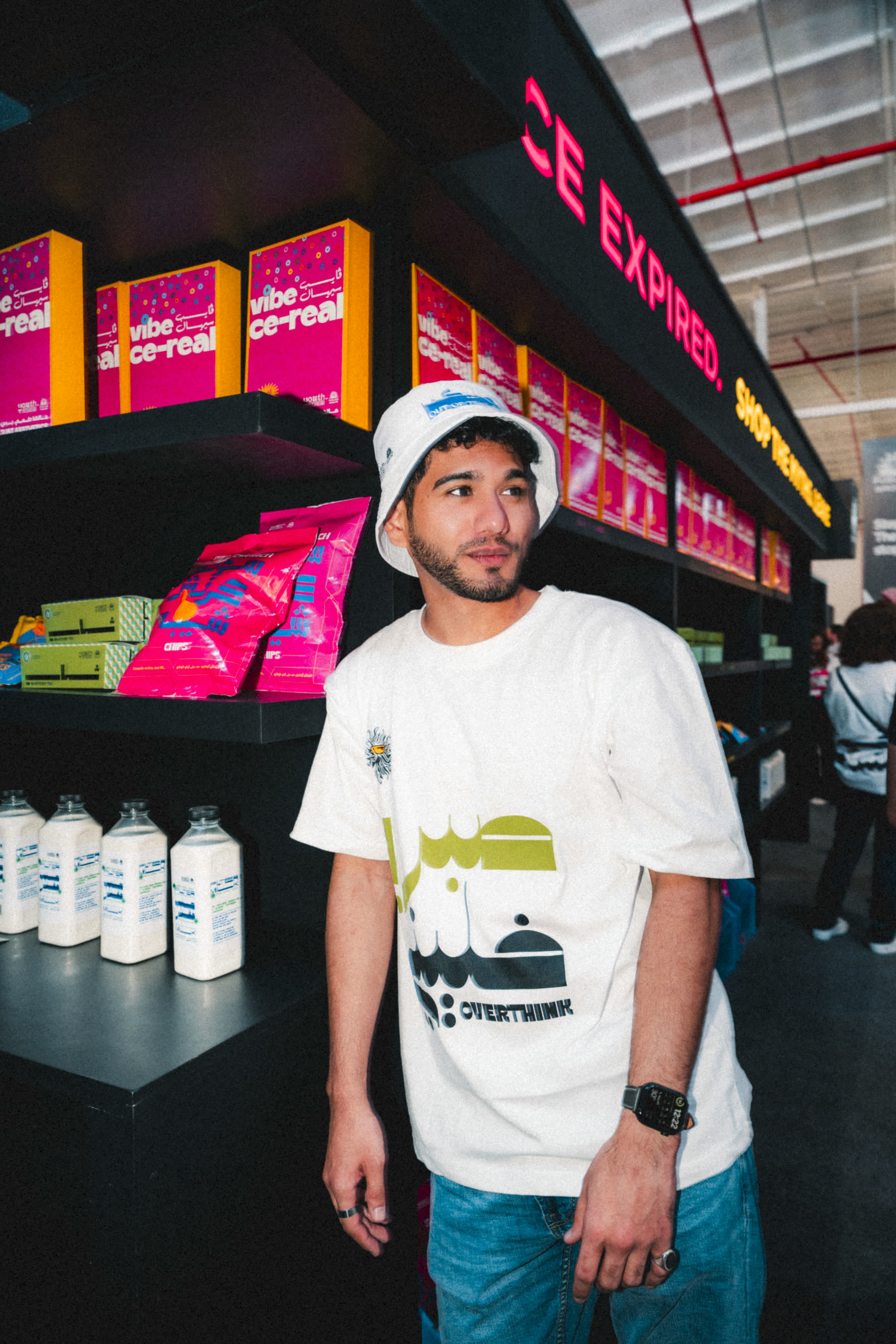 Visitor in a Youth Studio bucket hat and overthink tee in front of the shelves